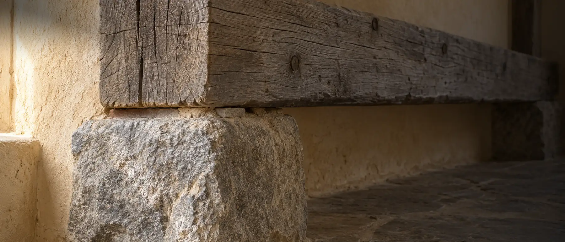A weathered timber beam bearing on a rough stone footing, shadow pooling under the joint