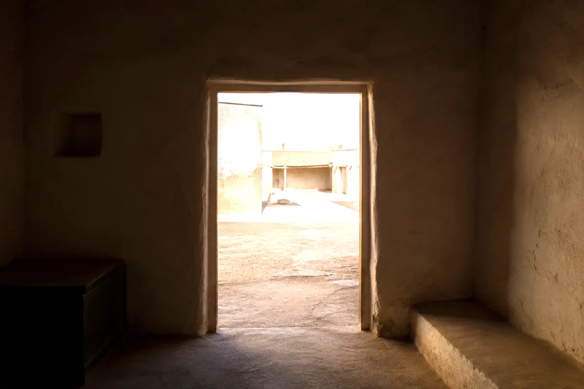 An open doorway seen from a dim room, giving onto a sunlit courtyard